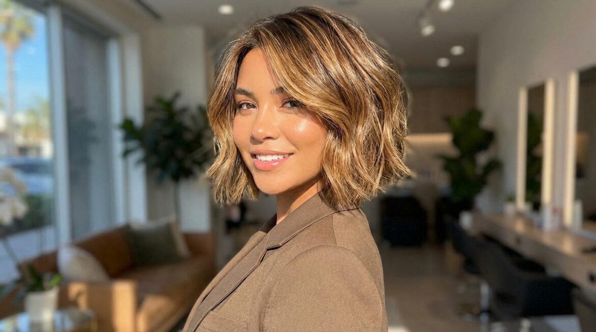 Femme souriante avec un carré court ondulé aux mèches blondes et caramel, dans un salon lumineux.