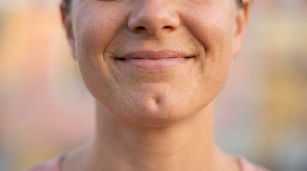 Gros plan sur une femme souriante, montrant clairement une fossette au menton. La peau est saine, l'expression est douce.