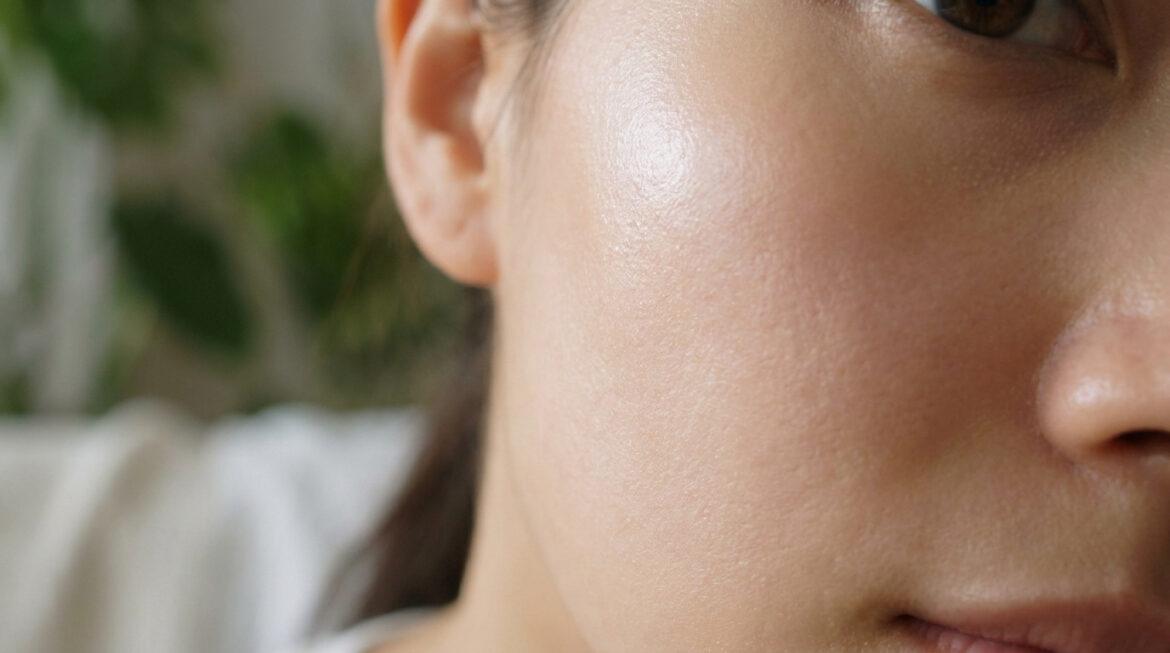 Gros plan sur le visage d'une personne, montrant une peau saine et lumineuse avec un léger éclat. Fond vert flou.